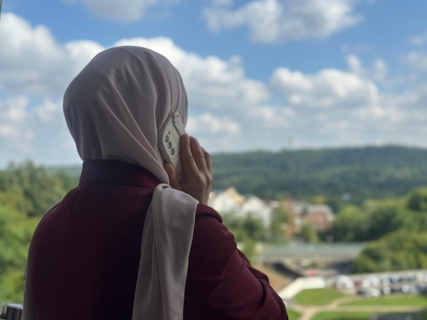 A woman wearing a headscarf is talking on a mobile phone, her face turned away from the camera. She is looking at a wide landscape. Photo by tuenews INTERNATIONAL.