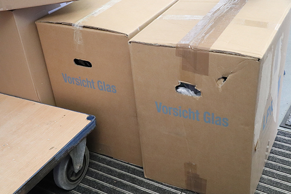 Drei hellbraune Umzugskartons mit einem Rollwagen davor.