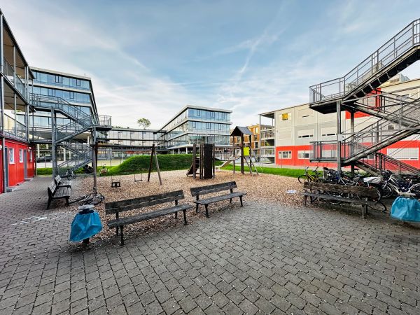 Blick in den Innenhof der Geflüchteten-Unterbringung in der Tübinger Wilhelm-Keil-Straße. Zu sehen sind Wohncontainer, Treppenanlagen, Spielplat-geräte, Bänke und abgestellte Fahrräder. In Hintergurnd ist das Landratsamt Tübingen.