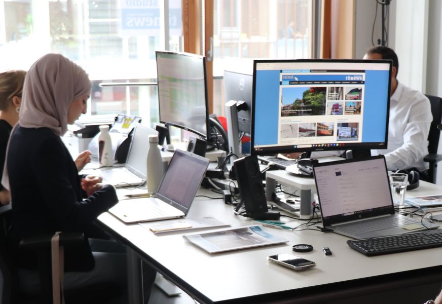 Mehrere Menschen sitzen an Computern und Bildschirmen im Büro.
