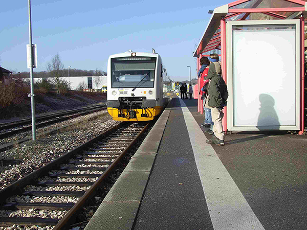 Ein Triebwagen der Schönbuchbahn fährt in den Bahnhof von Dettenhausen ein. Auf dem Bahnsteig stehen Menschen.