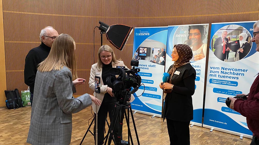 Das Foto zeigt 4 Menschen mit einer Fernsehkamera und Bildschirm vor RollUps über tuenews INTERNATIONAL