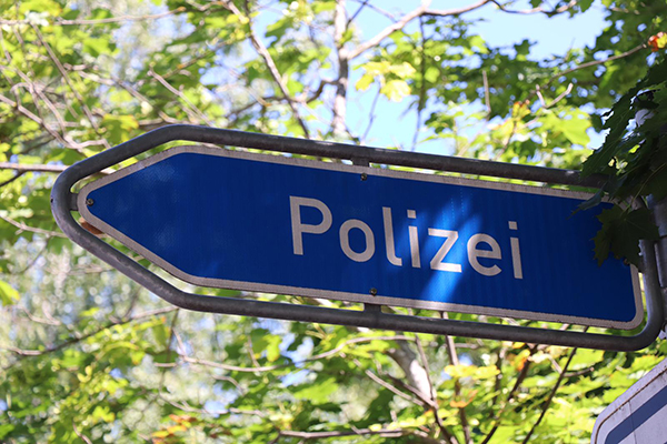Ein Verkehrsschild, dass den Weg zu einer Polizeistation weist. Unter sonnendurchfluteten Blättern.