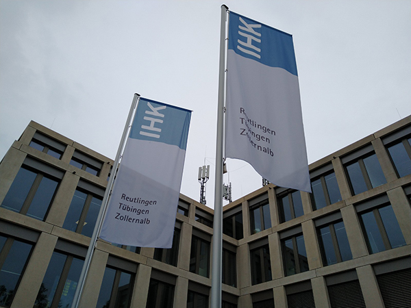 Ein mehrstöckiges Bürogebäude mit vielen Fenstern, davor zwei Fahnenmasten mit Flaggen der IHK Neckar-Alb.